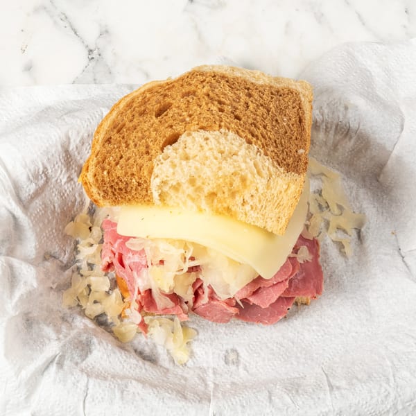 A partially assembled Reuben sandwich with corned beef, Swiss cheese, and sauerkraut on rye bread.