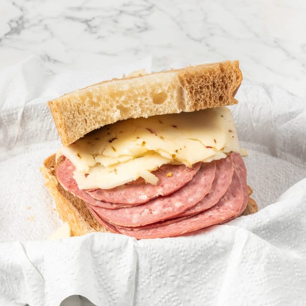 A sandwich with salami and cheese on light bread, served in a white paper-lined basket.