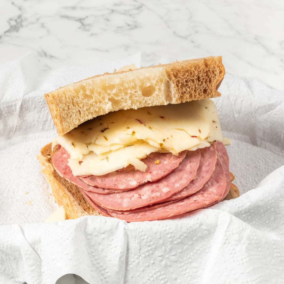 A sandwich with salami and cheese on light bread, served in a white paper-lined basket.