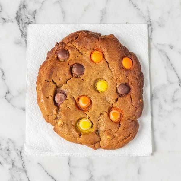 A large, round cookie with colorful candy-coated chocolate pieces on a white napkin.