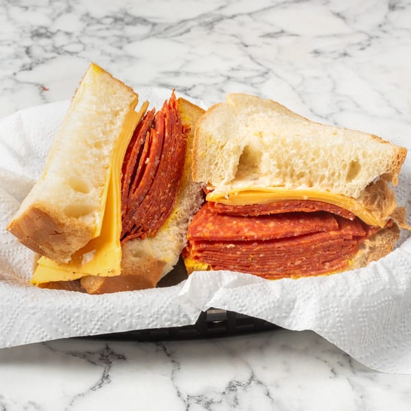 Two halves of a sandwich with salami, cheese, and mustard on white bread in a basket.