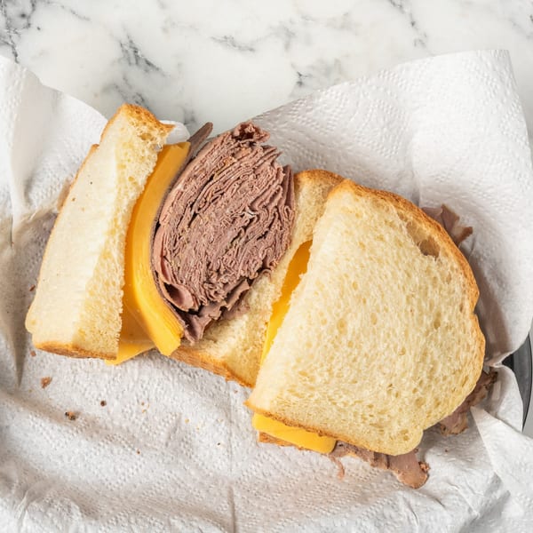 Top-down view of a roast beef and cheese sandwich on white bread, served on a paper towel.