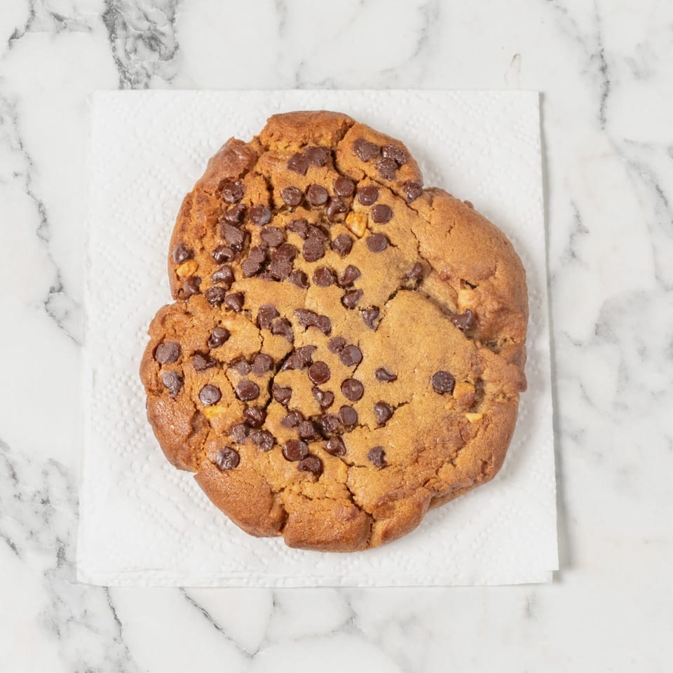 A large, golden-brown chocolate chip cookie with nuts rests on a white paper towel.