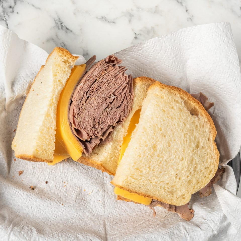 Top-down view of a roast beef and cheese sandwich on white bread, served on a paper towel.