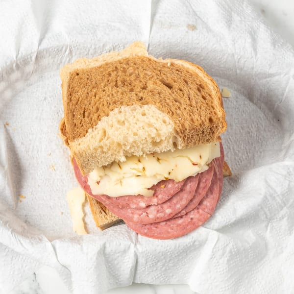 Salami and cheese sandwich on wheat bread, served on a white paper towel.